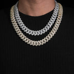 Two iced out Cuban link chain necklaces in silver and gold worn over a black shirt.
