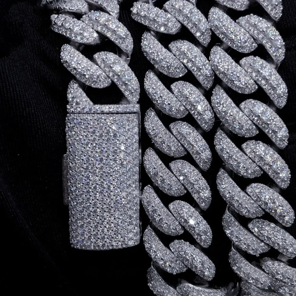 Close-up of a thick iced out Cuban link chain with sparkling stones on a black fabric background.